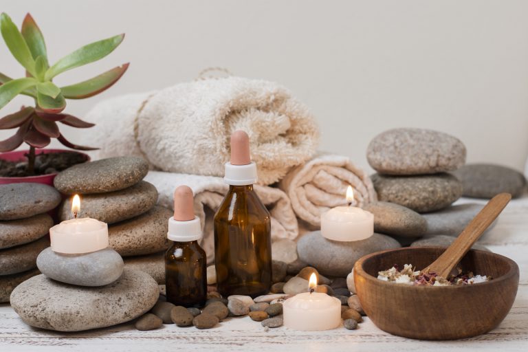 A relaxing Spa in Islamabad with stacked stones, glowing candles, essential oil bottles, soft rolled towels, and a bowl of soothing bath salts.